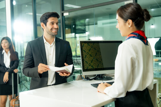 Airport staff assists a smiling passenger with travel documents at a modern check-in counter representing efficient service and a smooth journey.