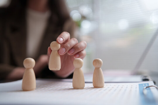 Recruiter choosing a wooden figure from candidates during hiring evaluation, representing recruitment, talent selection, human resources, employee screening and workforce planning.