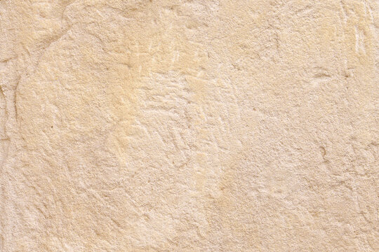 Beige weathered sandstone wall surface with natural rough grain texture and cracks. Abstract background of ancient stone architecture