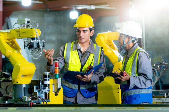 Industrial engineers inspect robotic machinery together while using a digital tablet to support efficient production monitoring and modern factory operations.