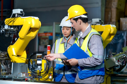 Industrial technicians examine robotic equipment while applying practical skills and reviewing technical details in a modern technology workplace.