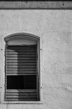 Arched Window with Broken Jalousies on a Stone Building Wall.