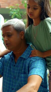 Indian Asian father repairing his child's bicycle on the house porch, with his son and daughter watching eagerly, while the wife looks on with a smile, capturing a happy family moment