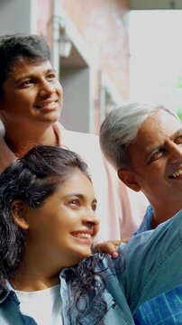 An Indian Asian family of four, parents in their forties and two kids, smiling while posing for a joyful portrait outside their lavish home, capturing a cherished moment together.