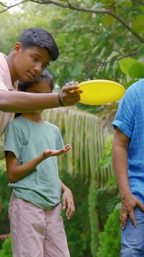 Indian Asian family of four spending quality time outdoors in their home lawn, parents in their forties watching as teenage son teaches his little sister how to throw a frisbee or flying disc