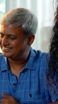 An Indian Asian family of four, with parents in their forties and two kids, enjoying a meal together at the dining table. The mother serves food while they talk and share happy moments