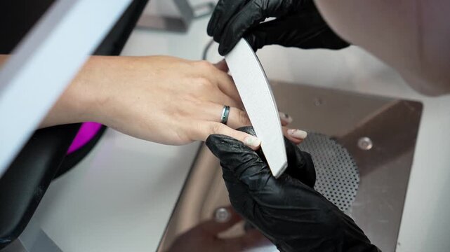 Nail technician files the edges of the nails during the final stage of a manicure. Professional finishing, nail shaping and beauty care concept