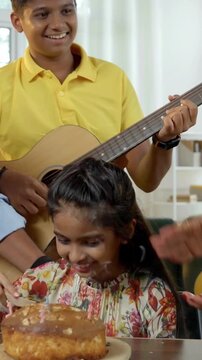 An Indian Asian family of four joyfully celebrates their small daughter's birthday by cutting a cake adorned with candles, surrounded by glitter, love, and laughter as they pose for a memorable photo