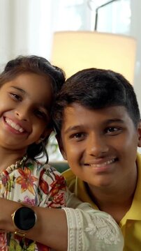 Indian Asian family of four, parents in their forties, sitting closely on a sofa with their two kids, smiling warmly while looking at the camera, capturing a joyful moment together indoors