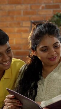 A closeup of a happy Indian Asian family consisting of parents in their mid-forties, a teenage son, and a small daughter joyfully reminiscing together while flipping through a cherished photo album