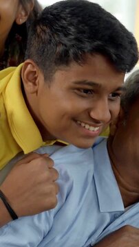 In this heartwarming closeup, an Indian Asian family of four shares a joyful moment, with the father in his forties leaning on the sofa, his kids and wife smiling and riding on her back 