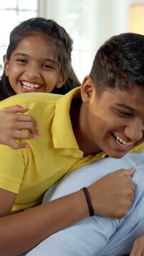 In this heartwarming closeup, an Indian Asian family of four shares a joyful moment, with the father in his forties leaning on the sofa, his kids and wife smiling and riding on her back 