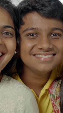 Indian Asian family of four, parents in their forties, sitting closely on a sofa with their two kids, smiling warmly while looking at the camera, capturing a joyful moment together indoors