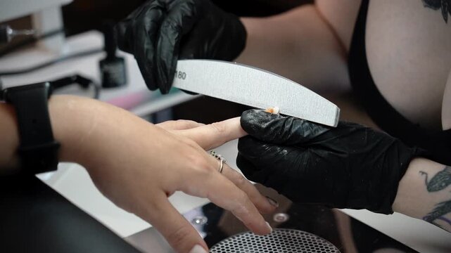 Nail technician files the edges of the nails during the final stage of a manicure. Professional finishing, nail shaping and beauty care concept