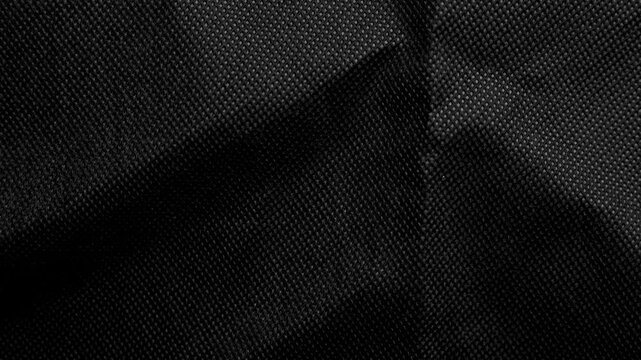 Abstract background of dark black crumpled fabric texture with elegant folds and fine woven textile pattern