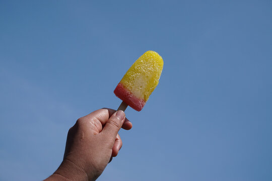 Hand holding a colorful fruit popsicle against a clear blue sky