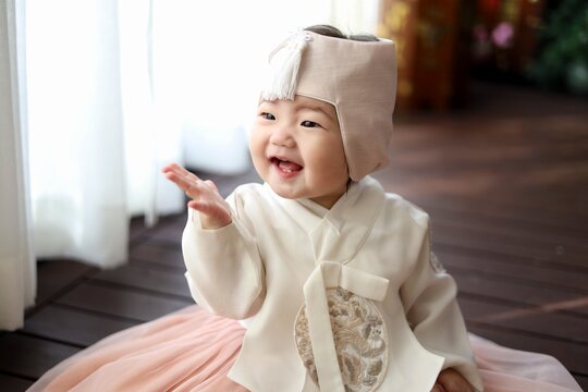 Adorable Asian baby smiling brightly and reaching out hand in traditional Hanbok 