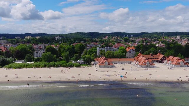 Aerial video showing the sandy beach of Sopot in Poland, coastline, historic architecture with red roofs, and people relaxing near the Baltic sea.