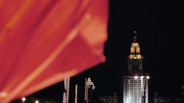 Moscow State University main building illuminated at night with red flag in foreground