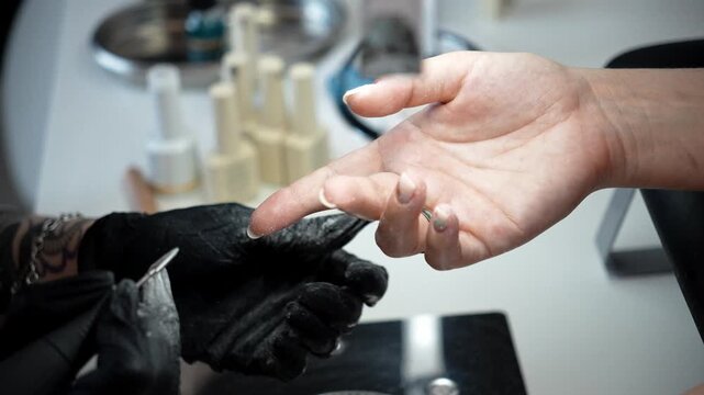Nail technician removes excess material from the underside of a shaped nail using an electric drill. Professional finishing and precise nail shaping concept
