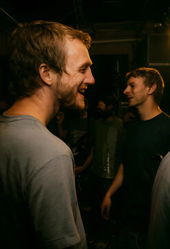 Smiling man with a beard laughing in a dimly lit social gathering, candid moment of joy and connection