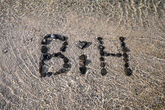 Stones arranged to spell BIH on a river bank splashed by water. Pebbles spelling the abbreviation for Bosnia and Herzegovina on the shore of a flowing river.