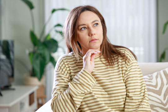Pensive woman sitting on sofa at home