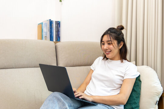 Young Asian woman smiling while using laptop on sofa at home
