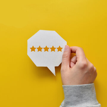 Hand holding five star rating speech bubble on yellow background