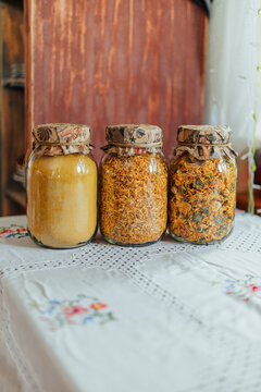 Three glass jars filled with golden dried flower petals, herbal material and fine yellow powder displayed on an embroidered tablecloth in a cozy home interior