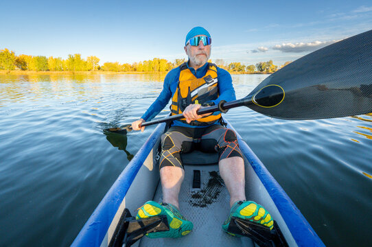 Senior male paddler in his 70s is paddling an inflatable touring kayak on a calm, serene lake in Colorado in fall scenery.