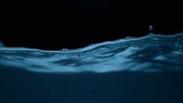 Dark ocean-blue water curls through continuous gentle currents, soft light revealing moving surface texture and subtle depth against near-black with calming natural atmosphere.

