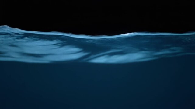 Dark ocean-blue water curls through continuous gentle currents, soft light revealing moving surface texture and subtle depth against near-black with calming natural atmosphere.