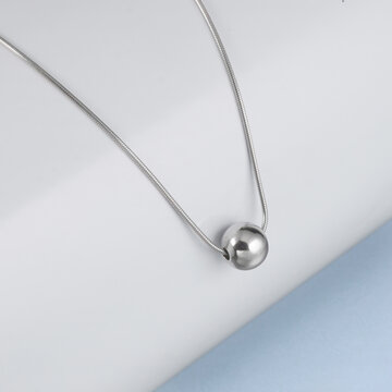 Minimalist silver ball pendant necklace resting on an elegant grey-blue textured background. Sophisticated lifestyle photography perfect for fashion and jewelry marketing.
