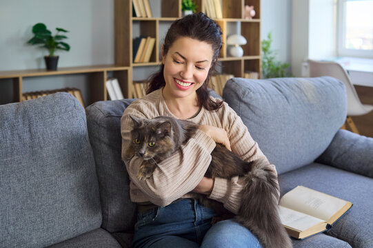 Woman and cat cuddle on home sofa. A cheerful owner hugs her pet with a warm smile, capturing genuine love and everyday companionship in a cozy living room. Concept of friendship and comfort.