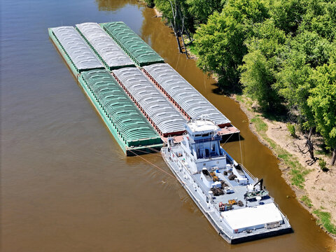  Aerial view of a tug boat with barges waiting outside the main channel next to the Mississippi shoreline.