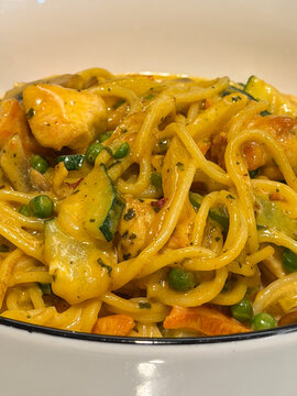 Creamy chicken pasta with zucchini peas and carrots in golden curry sauce served in white bowl