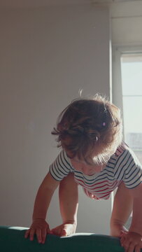 Toddler balancing on sofa before jumping, celebrating confidence, playful movement and adventurous childhood energy