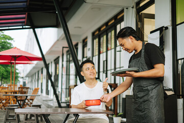 Fototapeta premium Smiling young Asian man giving thumbs up to server at outdoor cafe