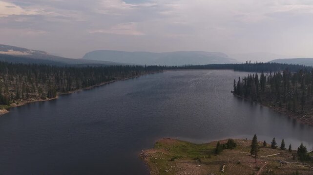 Aerial of alpine lake surrounded by forest and Uinta Mountains in Utah in summer under a cloudy sky