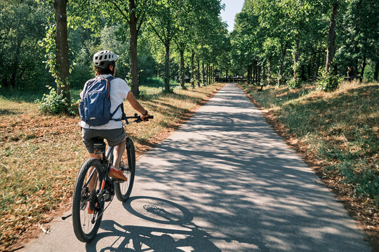 Active woman cycling on a sunny Sunday afternoon along a historic tree-lined avenue in Monrepos Park. Ludwigsburg, Baden-W&uuml;rttemberg, Germany.