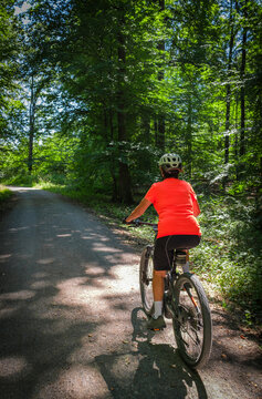 female Cyclist riding a bicycle along a peaceful forest avenue surrounded by lush green trees and dappled sunlight. Stuttgart, Baden-W&uuml;rttemberg, Germany.