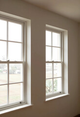 Fototapeta premium Two white sash windows with grid panes in a neutral room, natural light and interior design concept, the architectural elements provide a view to the outside