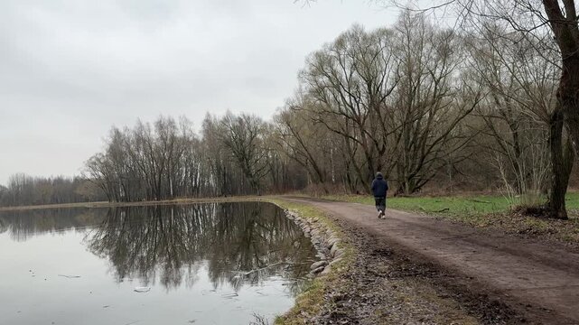 Quiet leafless trees and mirrorlike pond water under overcast sky, wide horizontal winter landscape with strong reflections, soft muted tones, and calm natural scenery for peaceful outdoor concepts