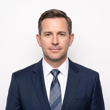 Professional headshot of a confident man in a dark blue suit and striped tie, looking directly at the viewer with a neutral expression.