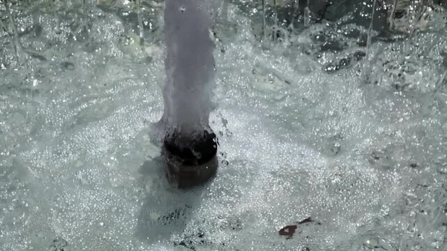 Slow-motion close-up shot of a water fountain nozzle jet shutting down, with splash, bubbles, and sparkling water droplets falling back into the pool.