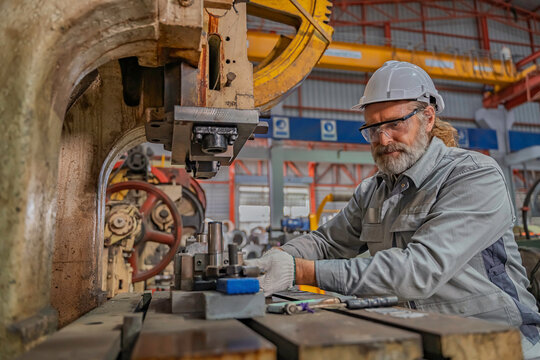 Industrial engineer inspecting heavy machinery during maintenance in a factory workshop. Focus on safety, precision, and mechanical engineering process for industrial equipment operation.