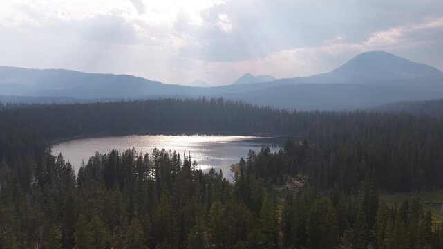 Aerial of alpine lake and mountains in Uinta Wasatch Cache National Forest in Utah with sunbeams breaking through cloudy skies