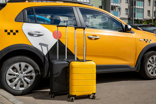 Yellow taxi car parked beside two suitcases on the street, showcasing urban environment with modern buildings in the background