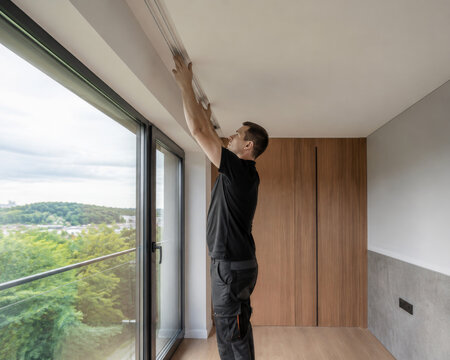 Un hombre trabaja en la instalaci&oacute;n de una l&aacute;mpara en un apartamento moderno con vista al paisaje